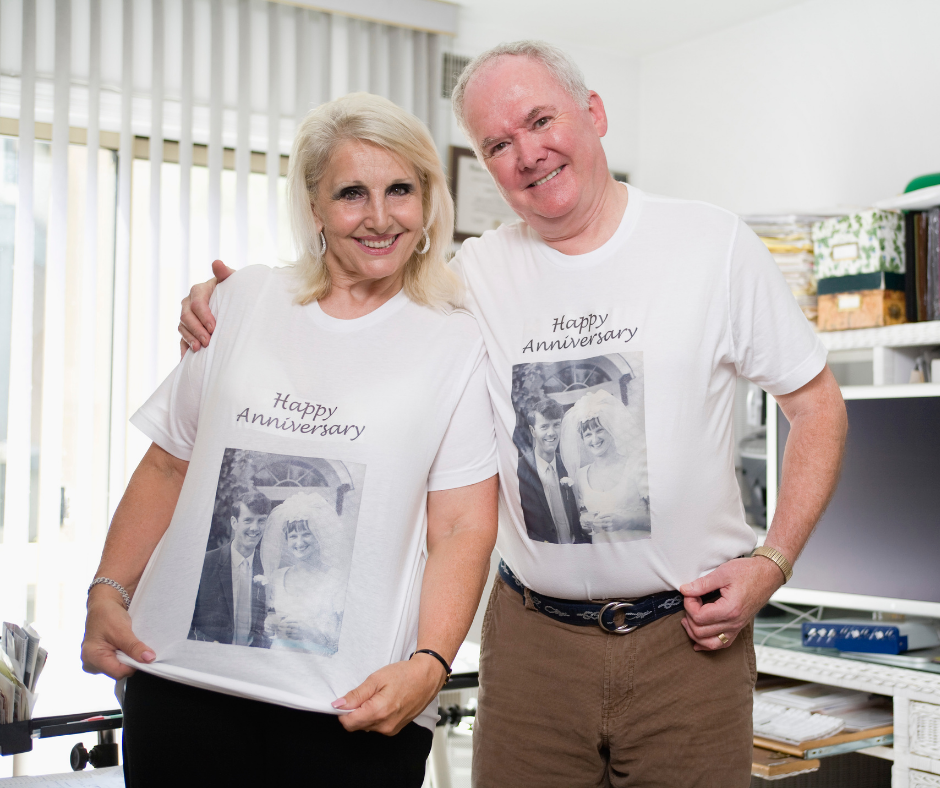An older couple wearing matching shirts with their wedding photo printed on it with the words "Happy Anniversary"
